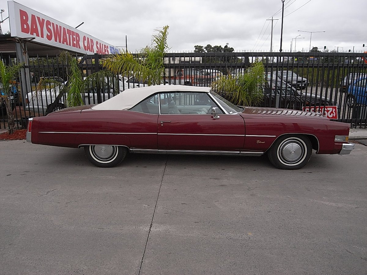 A maroon Cadillac Eldorado convertible parked under the Bayswater Car Sales sign
