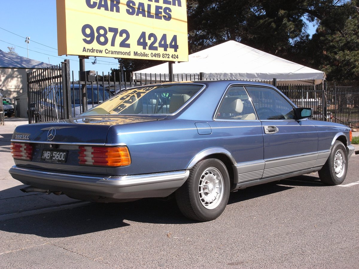 A Mercedes-Benz 380SEC parked under the large yellow Bayswater Car Sales roadside sign
