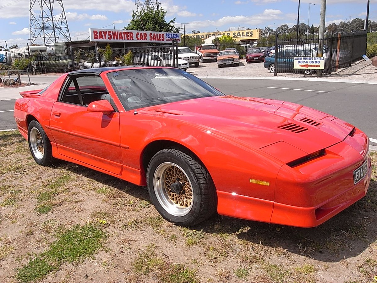 Several cars including a Pontiac Firebird Trans Am and a Cadillac parked in the yard, with the Bayswater Car Sales sign visible